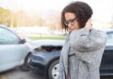 Young woman after being in a collision, holds her neck in pain