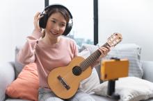 A girl plays a guitar while looking into a smart phone