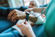 A health care worker puts a smartwatch for remote monitoring of vital signs on an elderly person