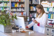 Young female pharmacist holding medication while using computer at pharmacy counter